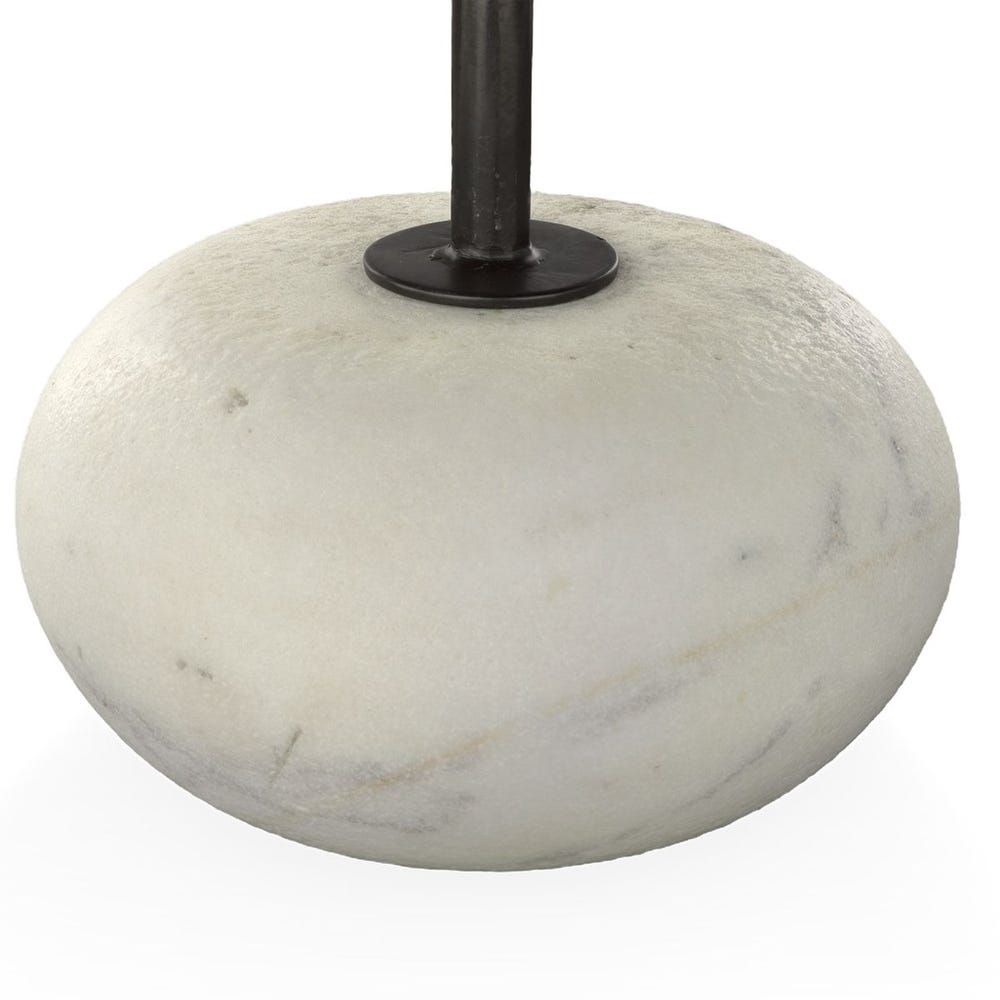 Detail of marble-like stone with a black metal stand on a white background. Round coffee table with hammered steel top and carved white stone base, styled in a sculptural modern living room with layered neutral textures.