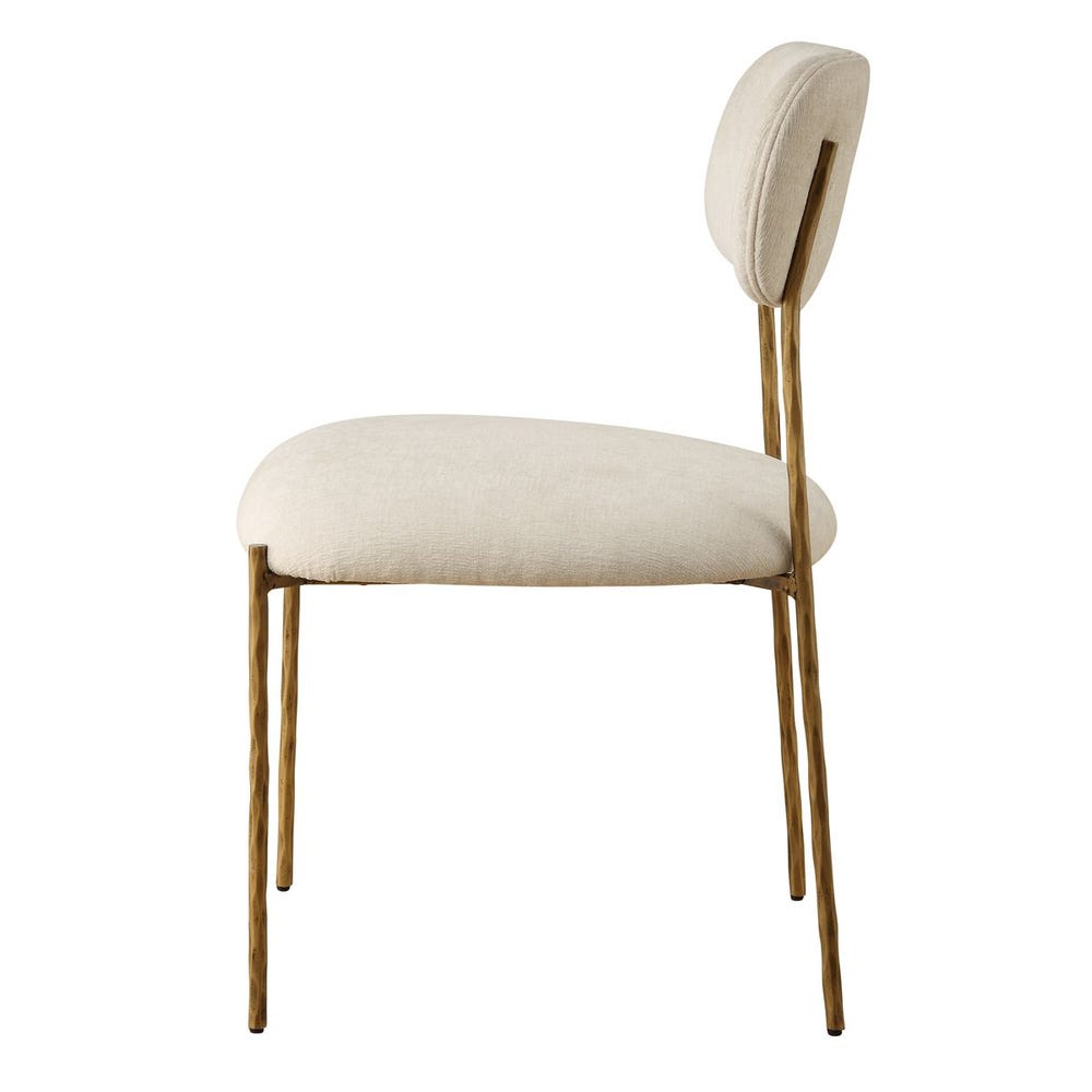 Sculptural iron dining chair with antique gold finish and floating off-white upholstered backrest.