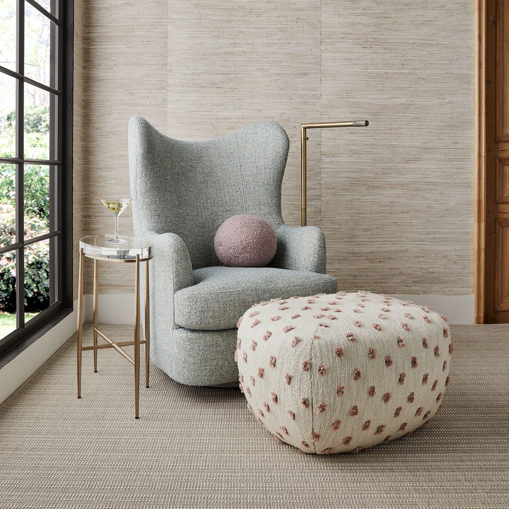 Gray armchair with a pink cushion and patterned ottoman in a room with large windows.