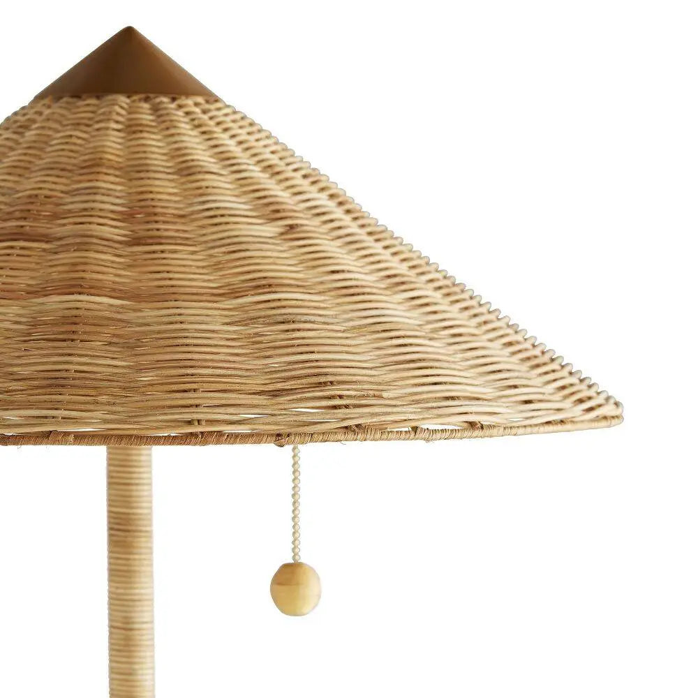Detail of tall rattan floor lamp with conical shade and antique brass base—coastal-inspired lighting with dual pull chains and warm, ambient glow.