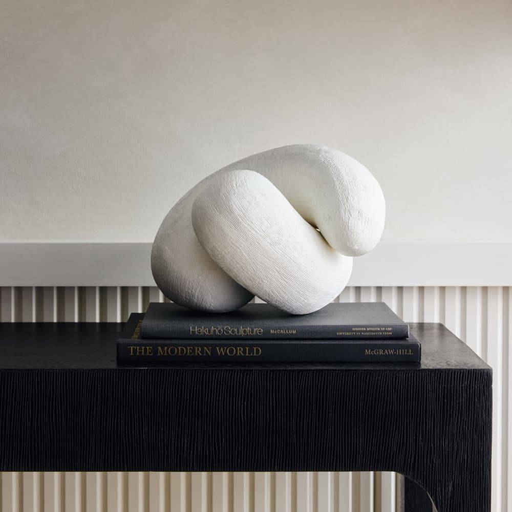 White interlocking knot sculpture styled on books on a black console