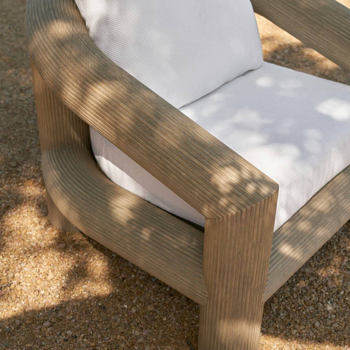 Close-up of the reeded teak arm and plush ivory cushions outdoors