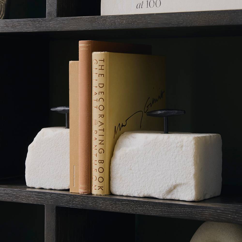 White marble block bookends holding design books on a dark bookshelf