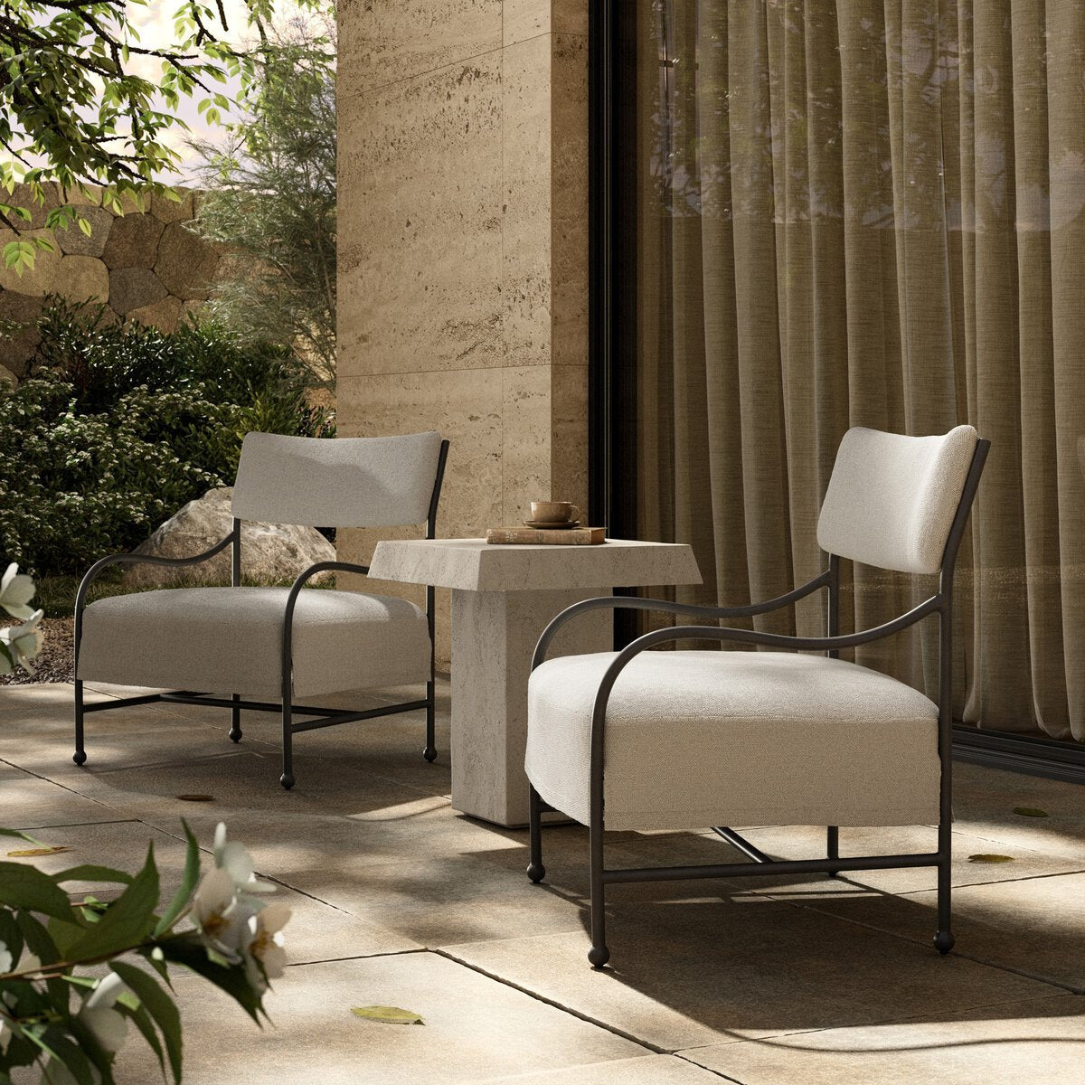 Two Solana outdoor lounge chairs with travertine side table on a stone patio — Rachel Blindauer furniture collection
