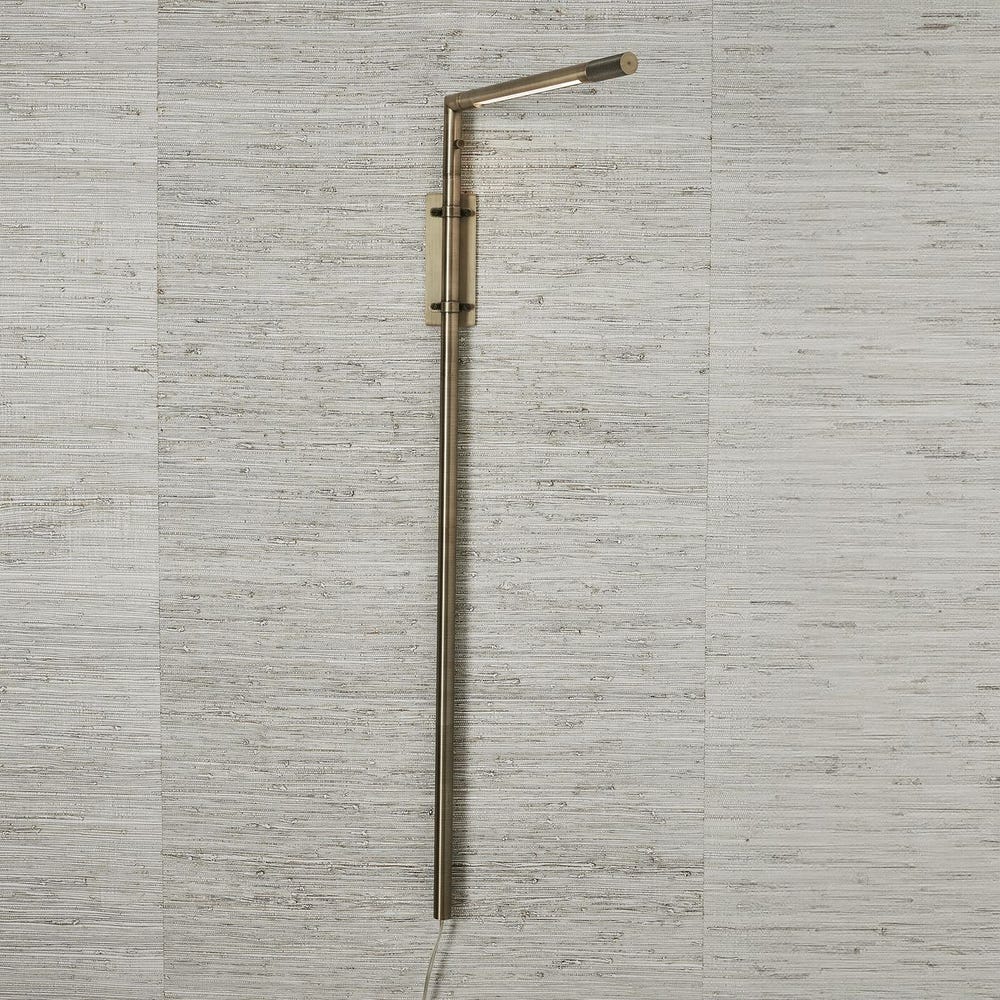 Antique brass wall sconce with adjustable rotating arm and integrated LED, styled in a minimalist reading nook for warm, directional lighting.