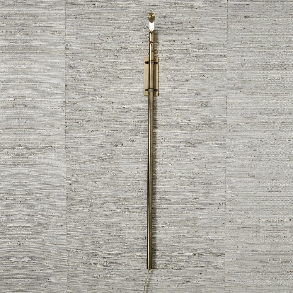 Antique brass wall sconce with adjustable rotating arm and integrated LED, styled in a minimalist reading nook for warm, directional lighting.