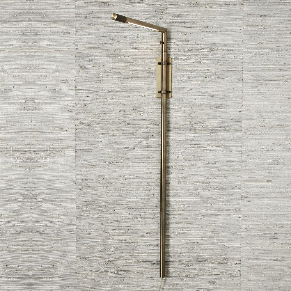 Antique brass wall sconce with adjustable rotating arm and integrated LED, styled in a minimalist reading nook for warm, directional lighting.