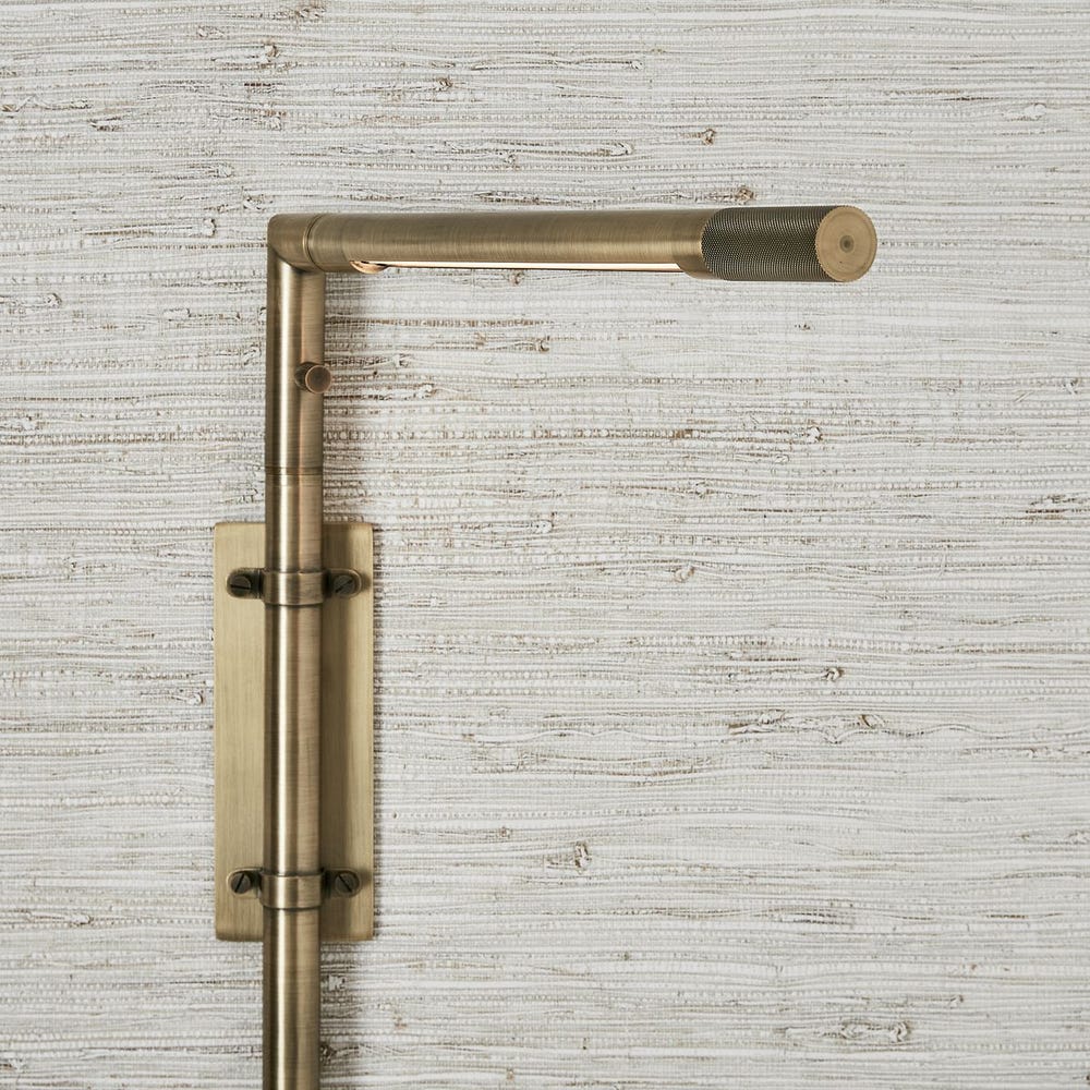 Antique brass wall sconce with adjustable rotating arm and integrated LED, styled in a minimalist reading nook for warm, directional lighting.
