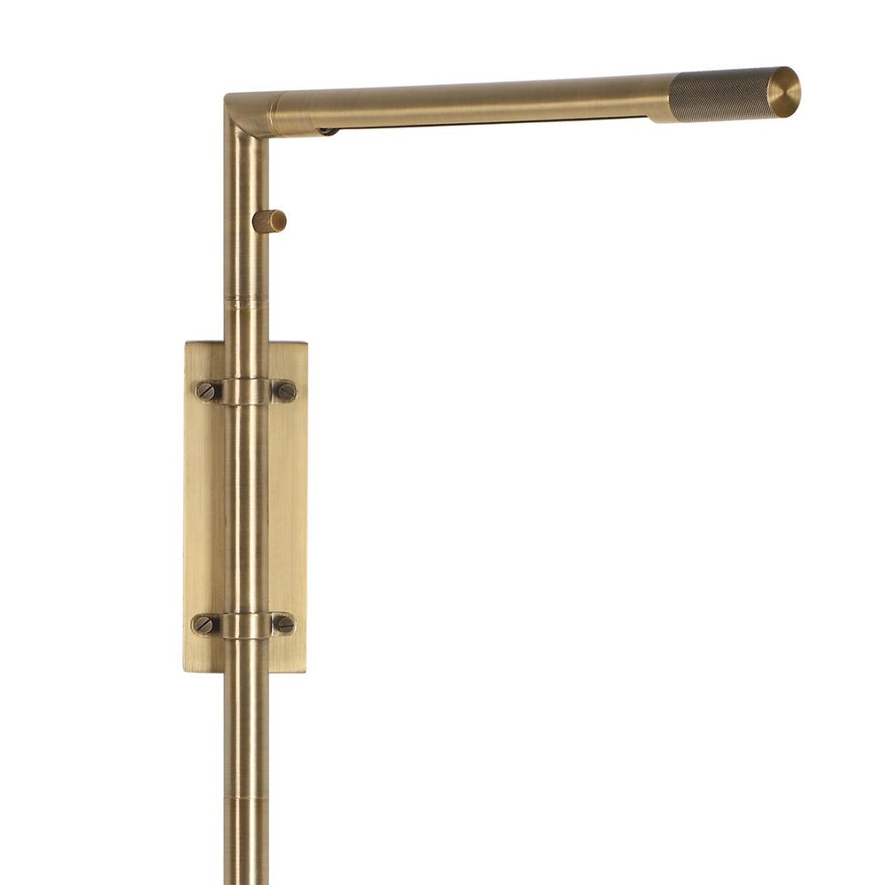 Antique brass wall sconce with adjustable rotating arm and integrated LED, styled in a minimalist reading nook for warm, directional lighting.