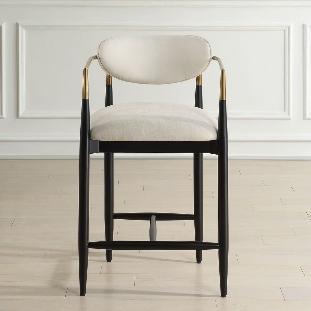 Mid-century modern counter stool with off-white velvet seat, matte black wood base, and brushed brass arms.