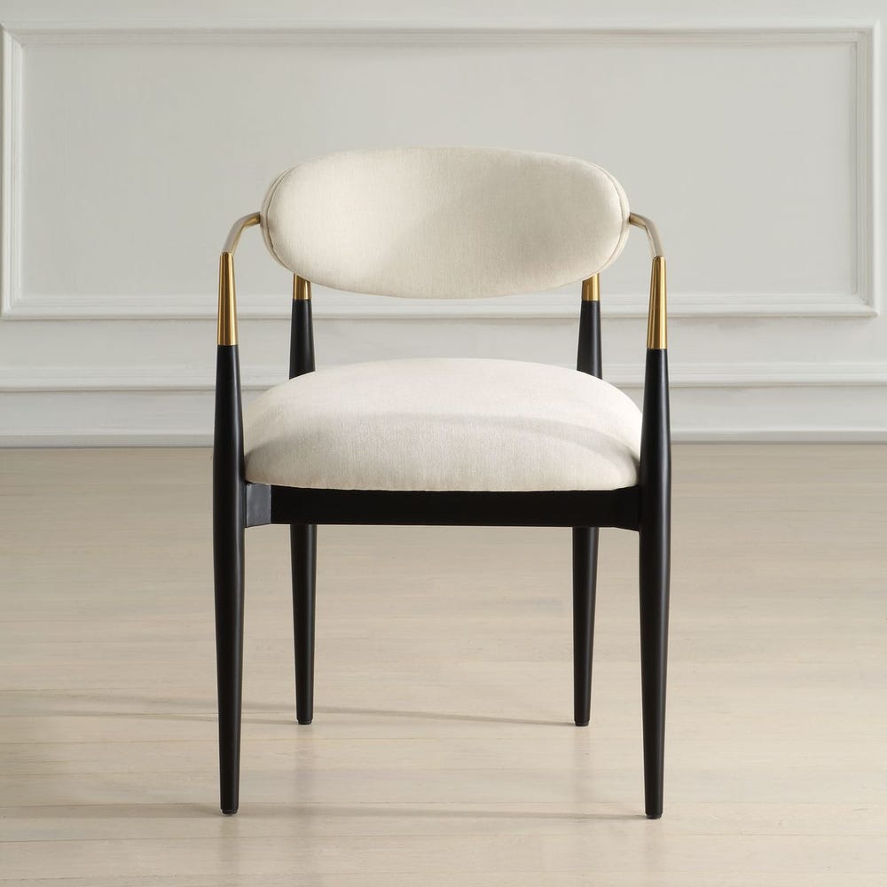 Mid-century modern dining armchair with off-white velvet upholstery, matte black wood legs, and brushed brass wraparound arms.