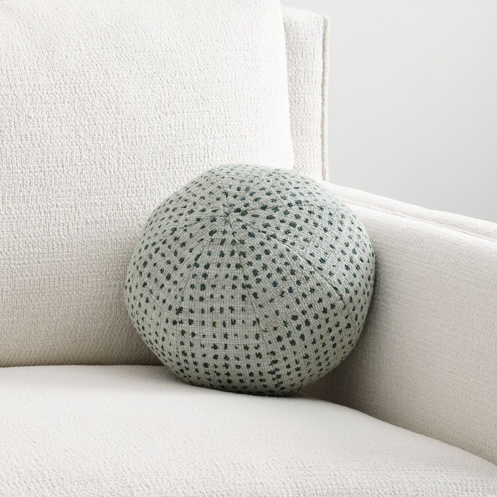 Round chenille ball pillow in sea salt and aqua dot pattern, styled on a sculptural lounge chair with neutral boucle upholstery.
