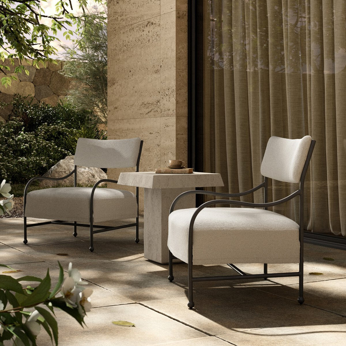 Outdoor lounge chair with curved matte gunmetal frame and handwoven linen-toned seat, styled for sculptural coastal living.