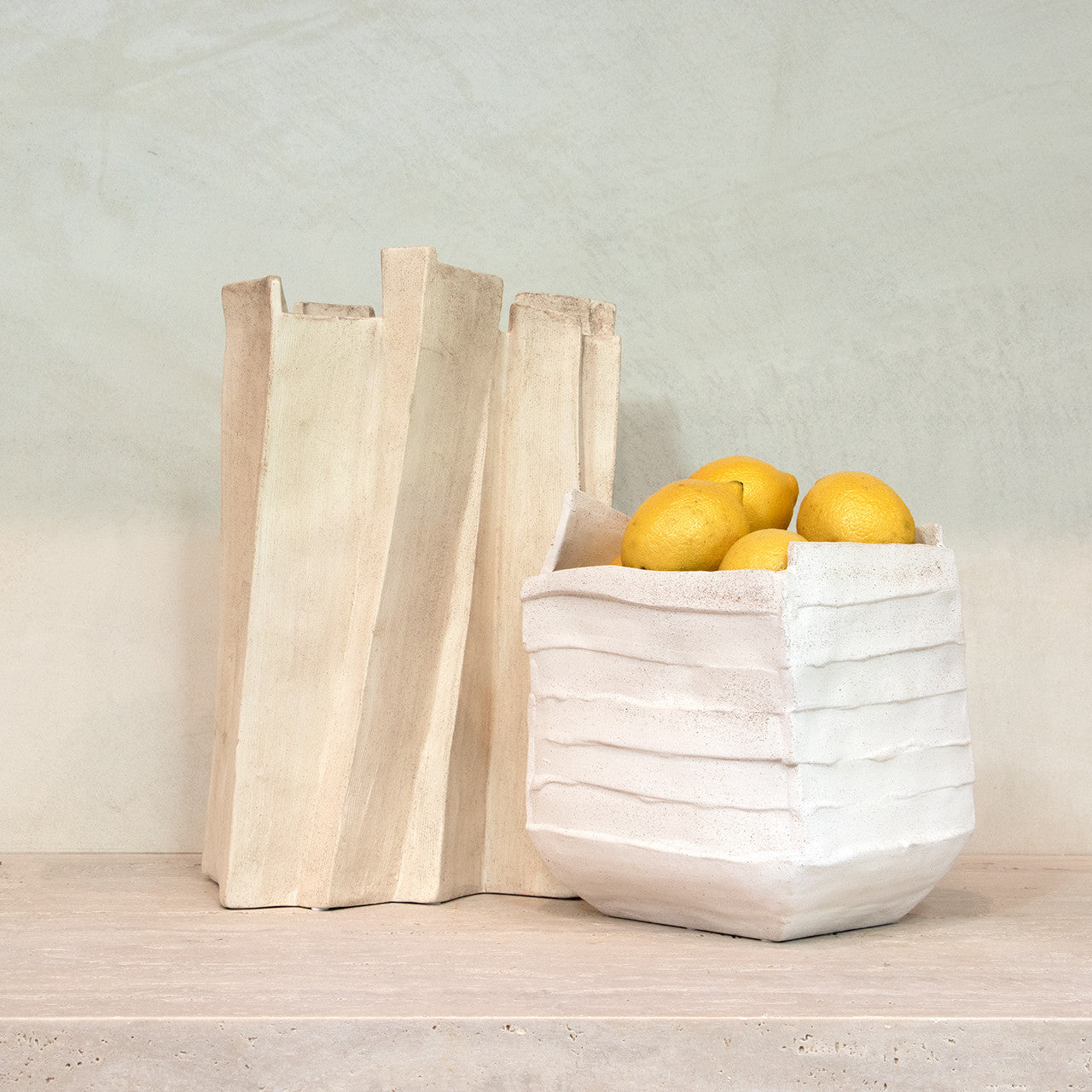 Modern sculptural vase in matte beige porcelain with folded ridges and rectangular form, styled as a standalone accent or with dried branches in minimalist interiors.