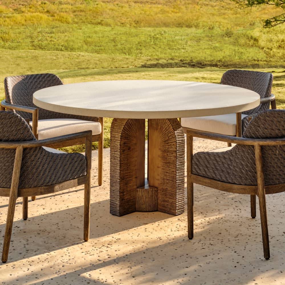 Round ivory outdoor dining table with woven chairs on a stone patio