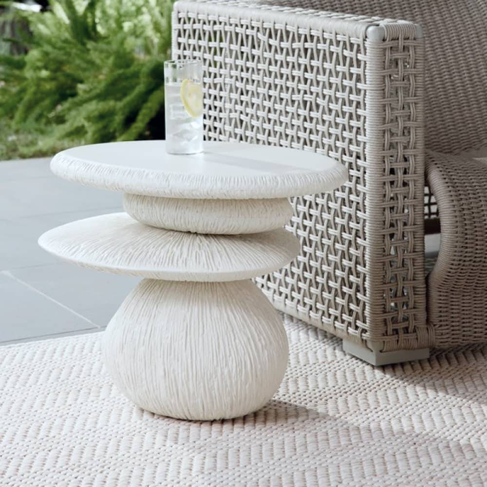 Ivory stacked stone side table beside a woven outdoor lounge chair
