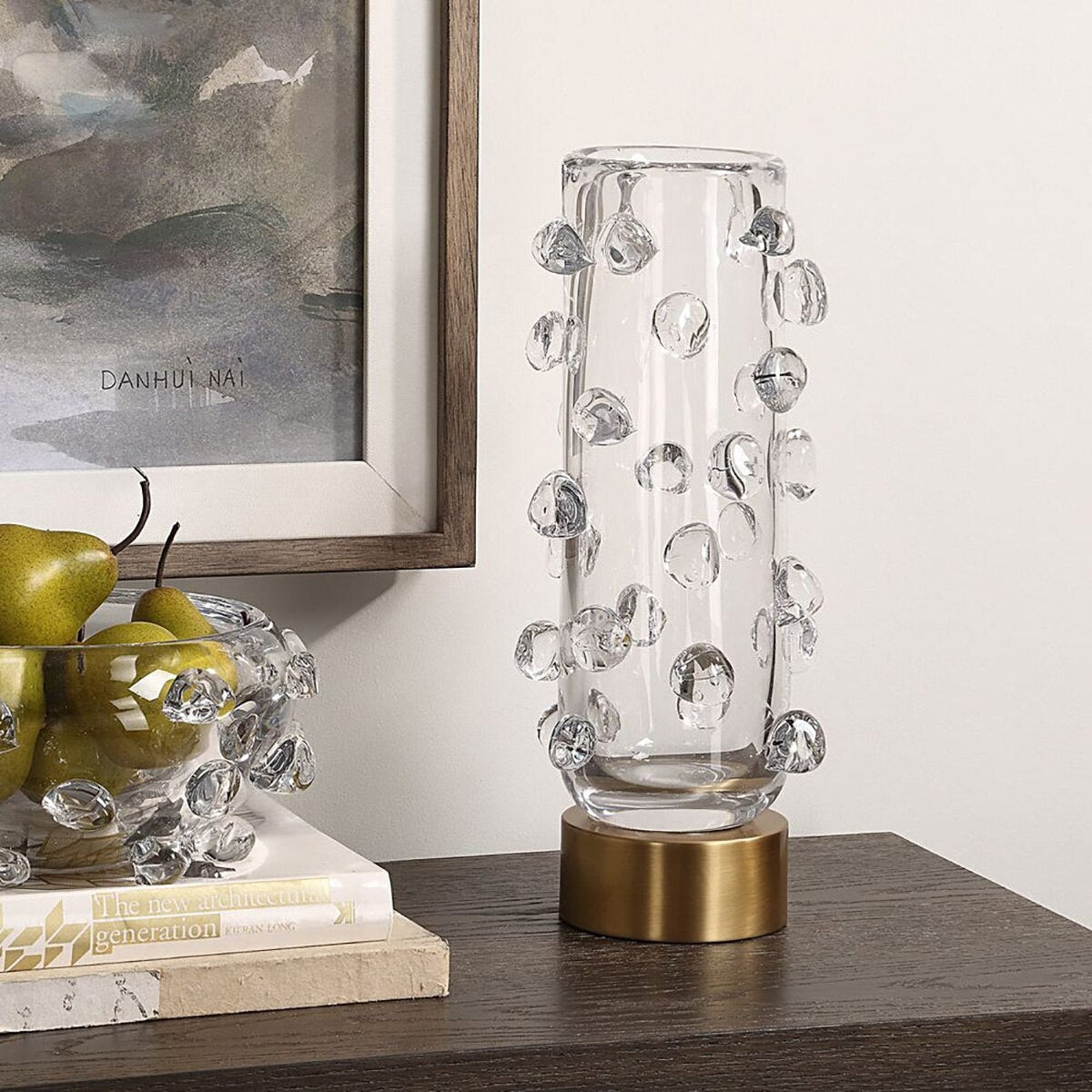 Clear glass droplet vase on a console beside a bowl of pears