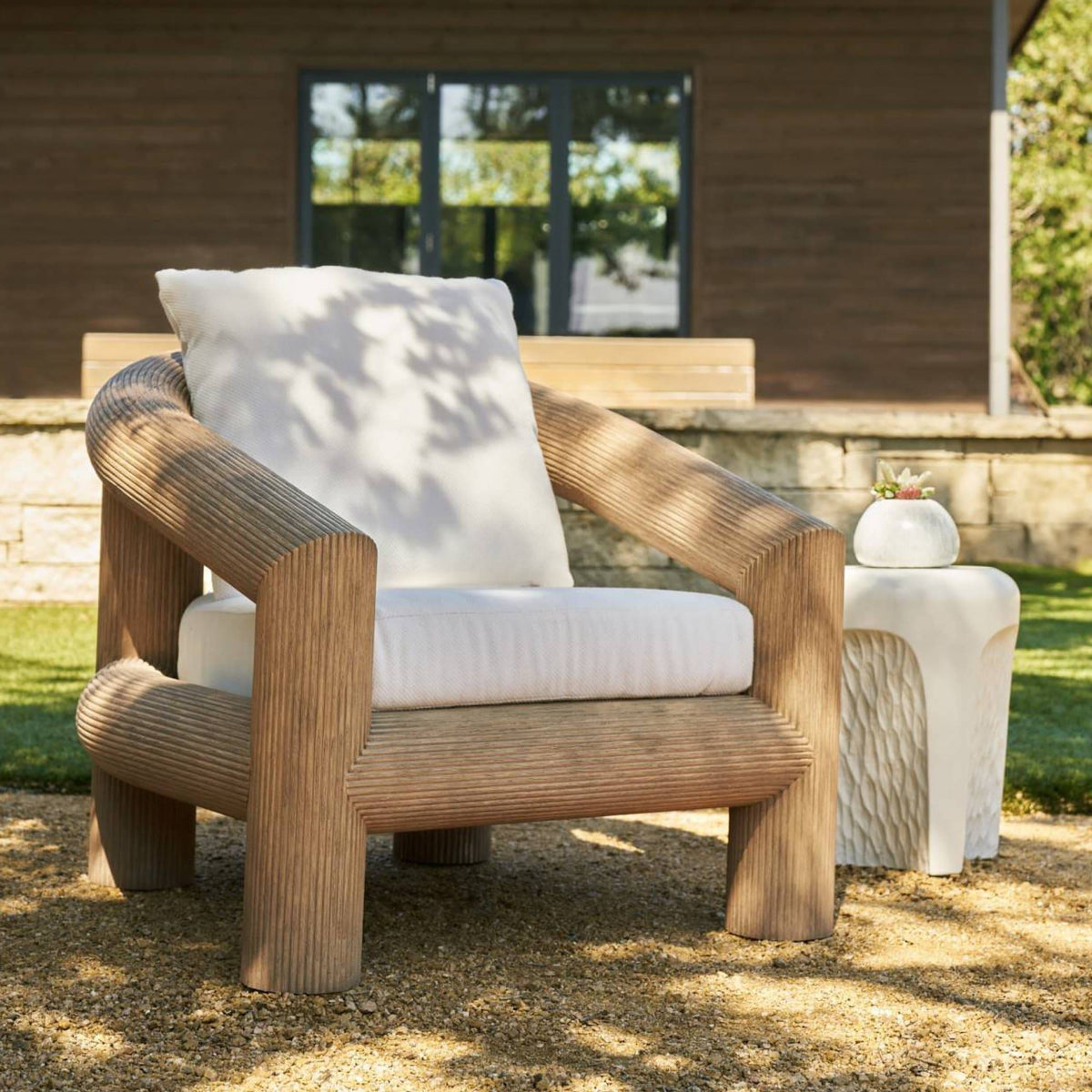 Oversized teak outdoor lounge chair with plush cushions in dappled sun