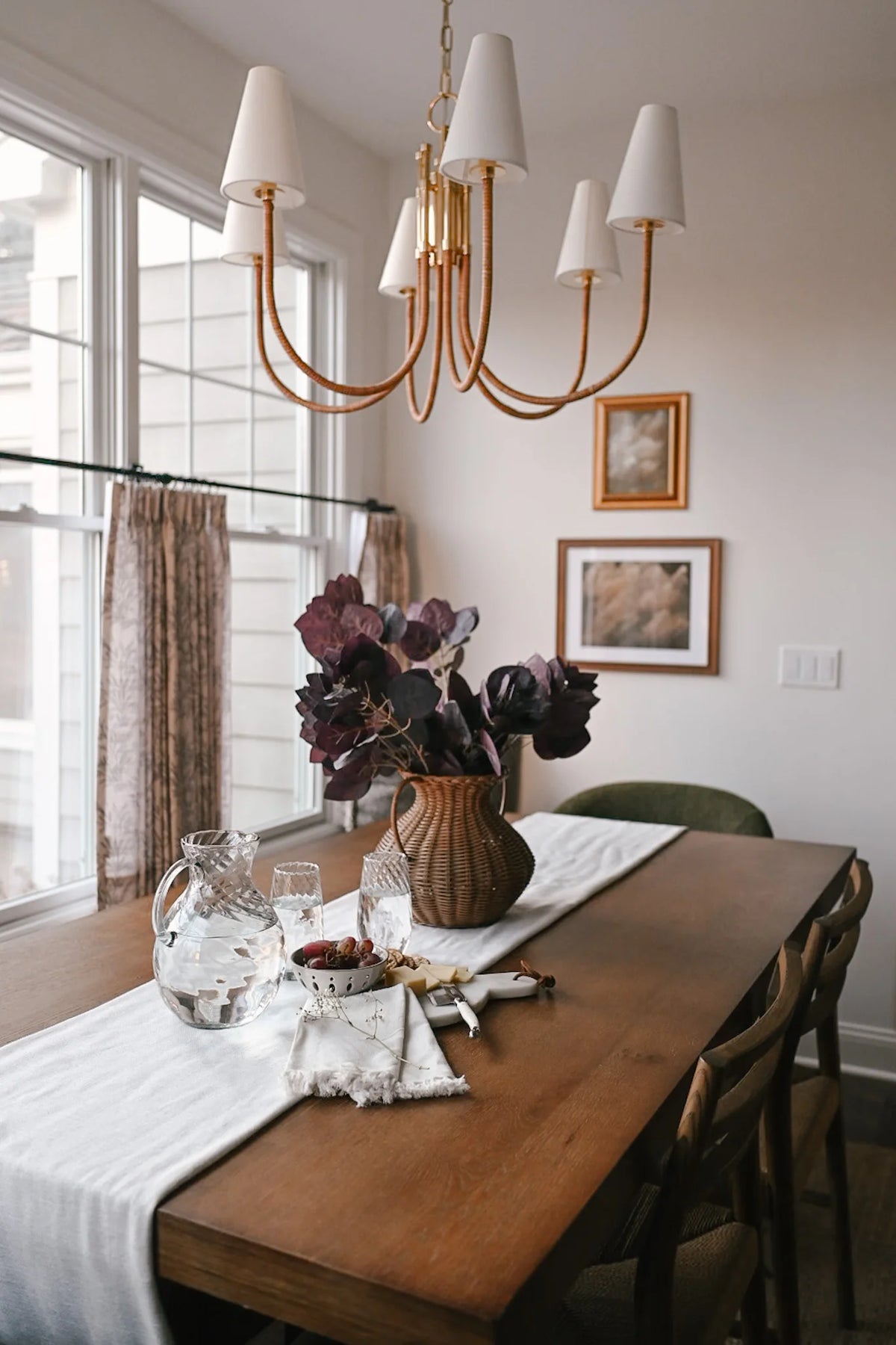 Dining room with a wooden table, Maris chandelier, and framed pictures on the wall.