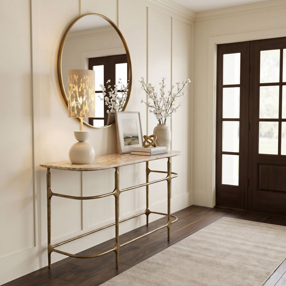 Brass and stone console table styled in a paneled entryway with a round brass mirror and blossoms