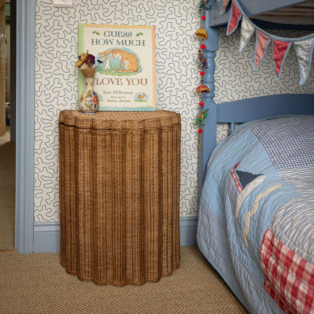 Oak rattan nightstand basket beside a bed with a blue quilt