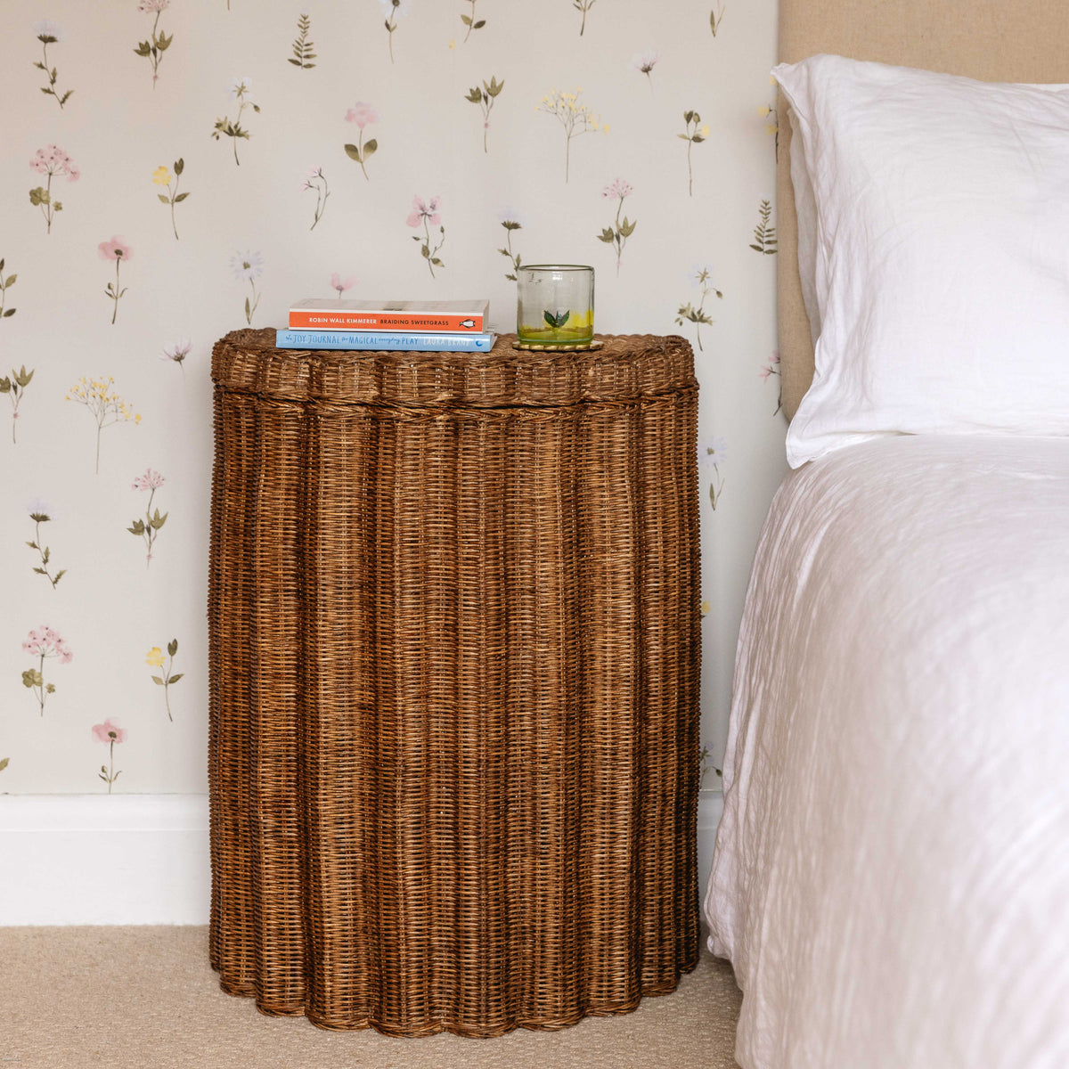 Scalloped rattan nightstand next to a bed with white linen