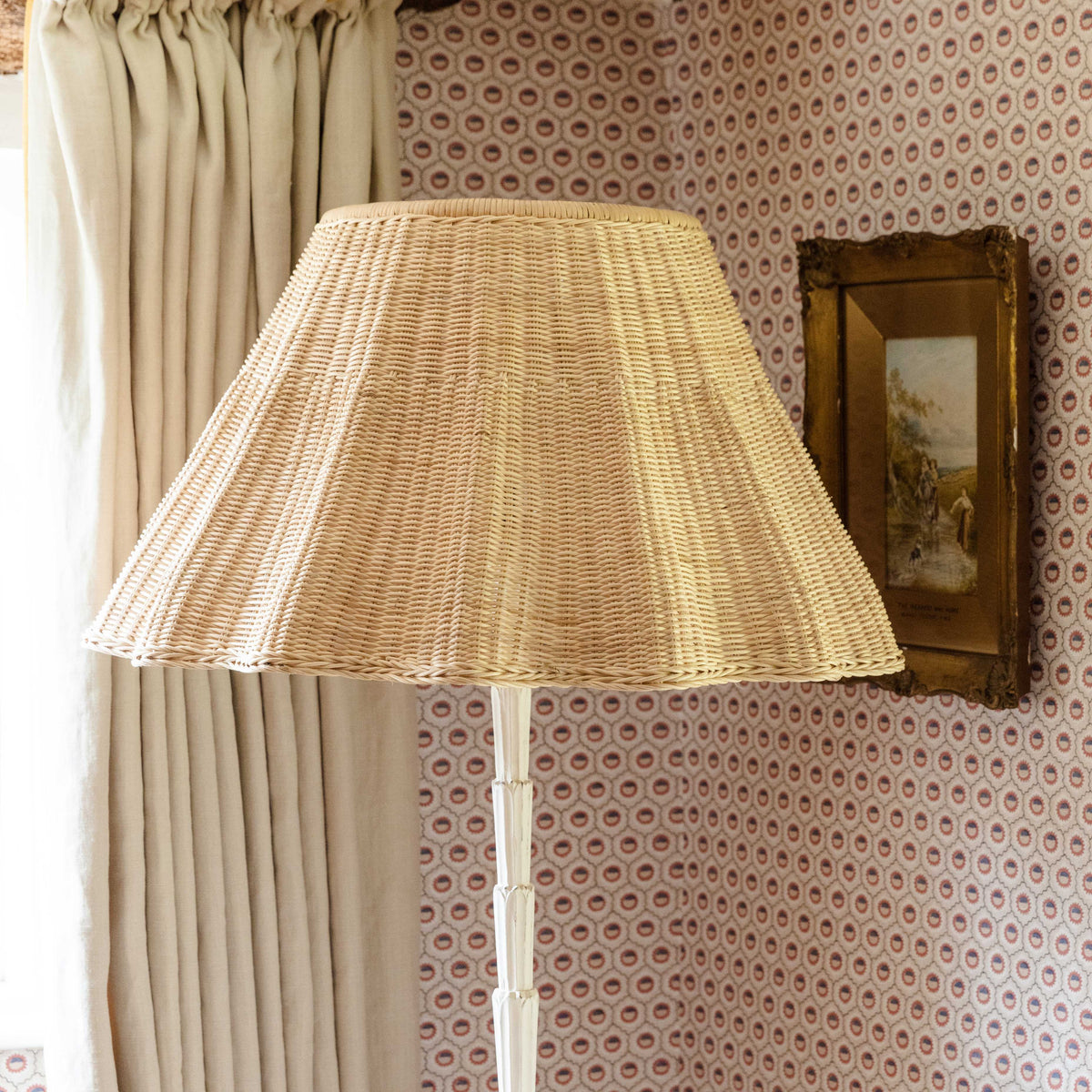 Rattan lampshade on a white floor lamp beside linen curtains